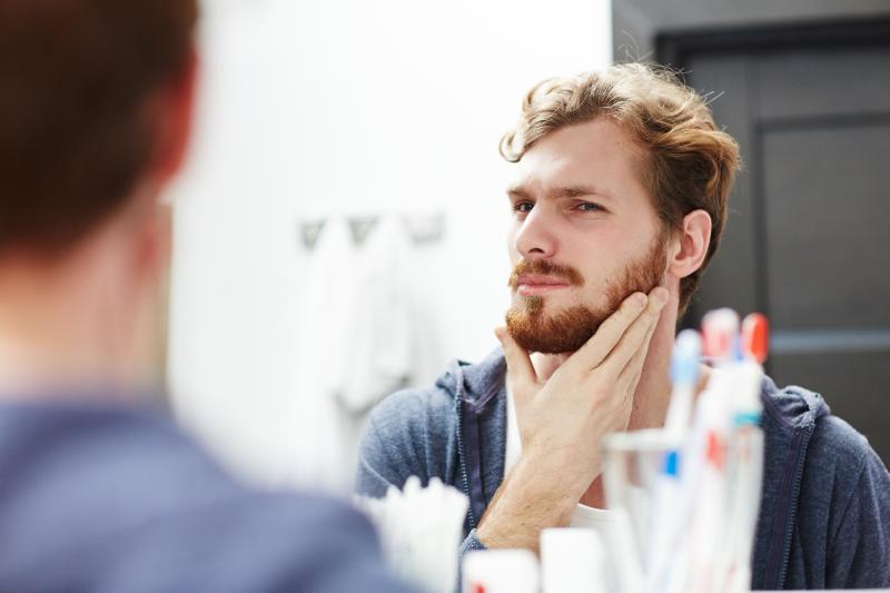 man checking for patches in his beard in a mirror